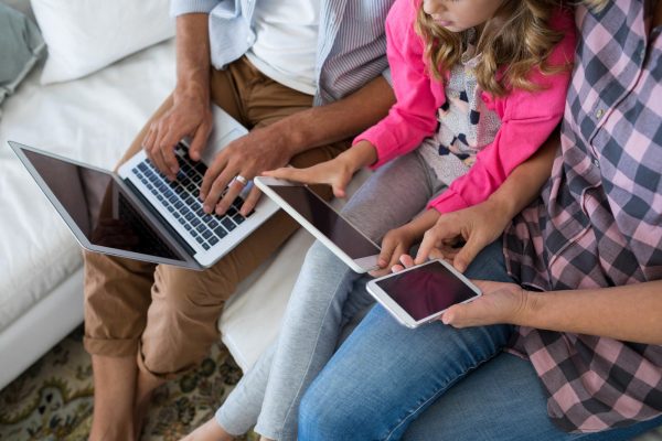 Family using laptop, digital tablet and mobile phone in living room